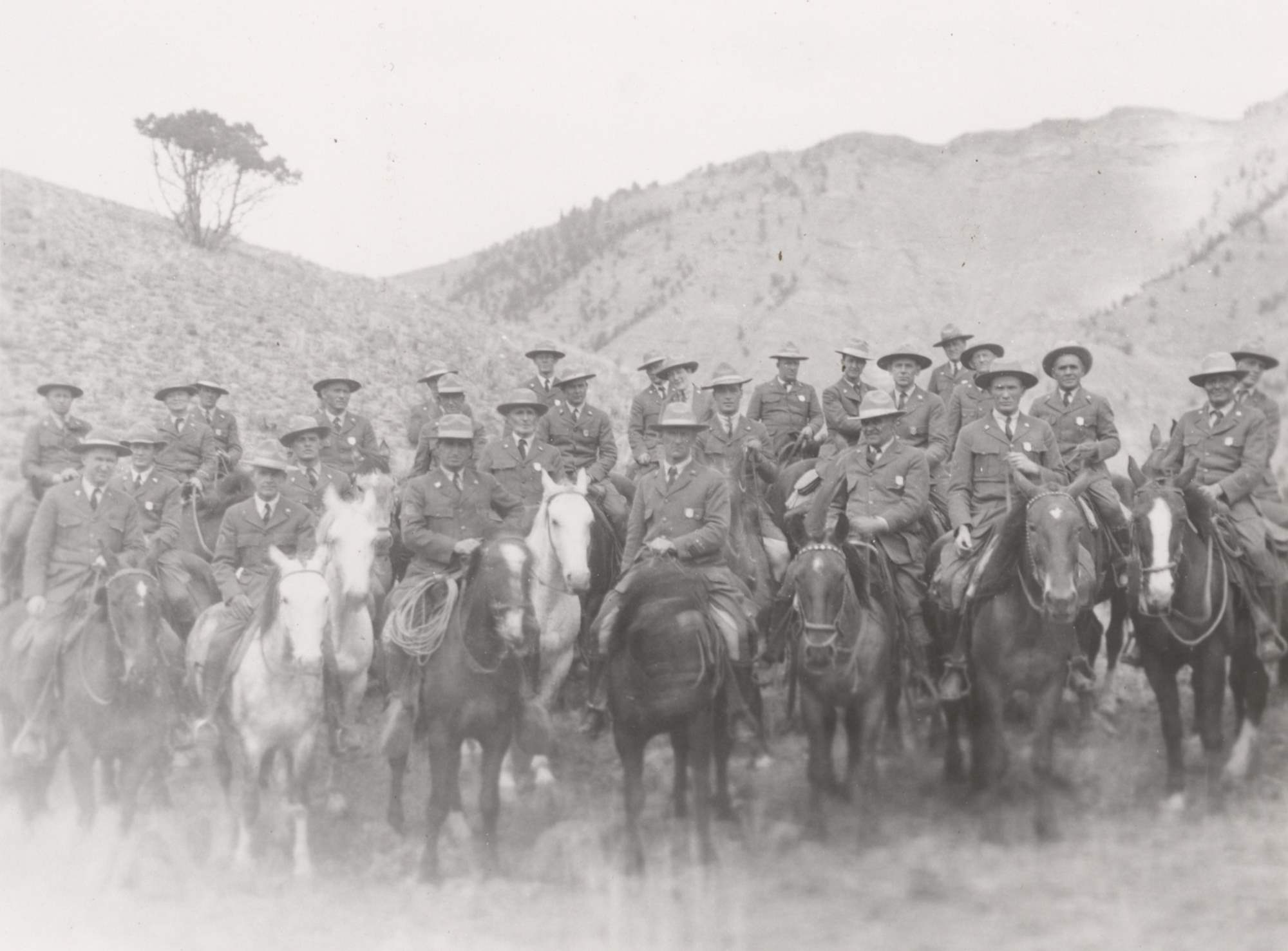 Twenty-seven men and one woman in NPS uniforms and broad brim hats pose on horses. Most wear shield-shaped badges.